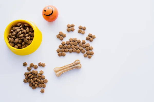 Vista superior da forma da pata feita de alimento seco para animais de estimação perto do osso e tigela isolada em branco — Fotografia de Stock