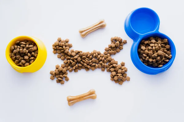 Vista superior da forma óssea feita de alimentos secos para animais de estimação perto de tigelas isoladas em branco — Fotografia de Stock