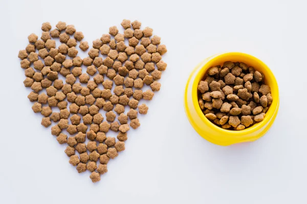 Vista superior de alimentos secos para animais de estimação em forma de coração e tigela isolada em branco — Fotografia de Stock