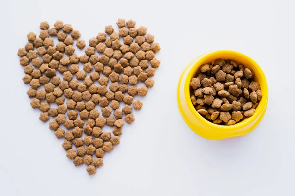 Vista dall'alto del cibo secco per animali domestici a forma di cuore e ciotola isolata su bianco — Foto stock