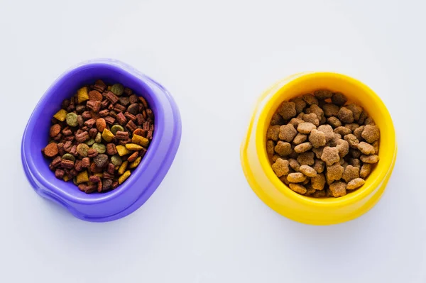 Vue de dessus des bols en plastique avec différents aliments pour animaux isolés sur blanc — Photo de stock