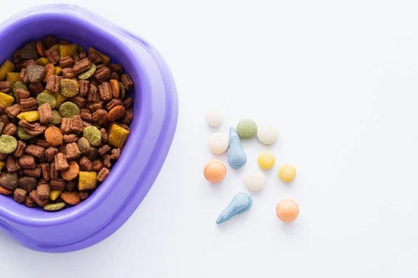Top view of plastic bowl with dry pet food near vitamins in pills isolated on white — Stock Photo