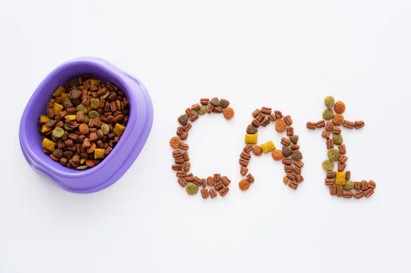 Vista superior da palavra do gato feita de alimento seco para animais de estimação perto da tigela isolada no branco — Fotografia de Stock