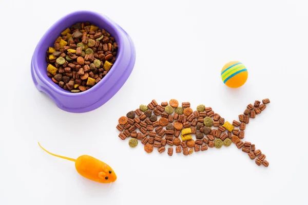 Forme de poisson fait avec de la nourriture sèche pour animaux de compagnie près bol violet et jouets isolés sur blanc — Photo de stock