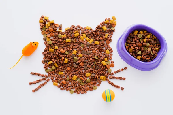 Vista superior de la forma del gato hecha de comida seca para mascotas cerca de un tazón y juguetes aislados en blanco - foto de stock