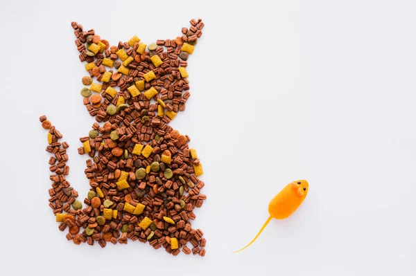 Vista superior da forma do gato feito a partir de alimentos secos para animais de estimação perto de rato de borracha isolado em branco — Fotografia de Stock
