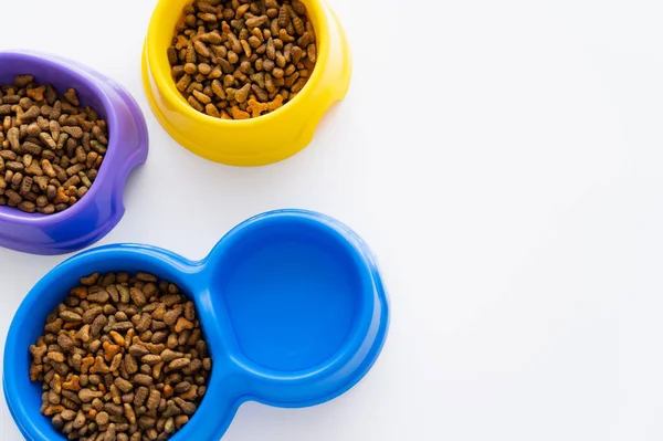 Top view of water near colorful bowls with dry pet food isolated on white — Stock Photo