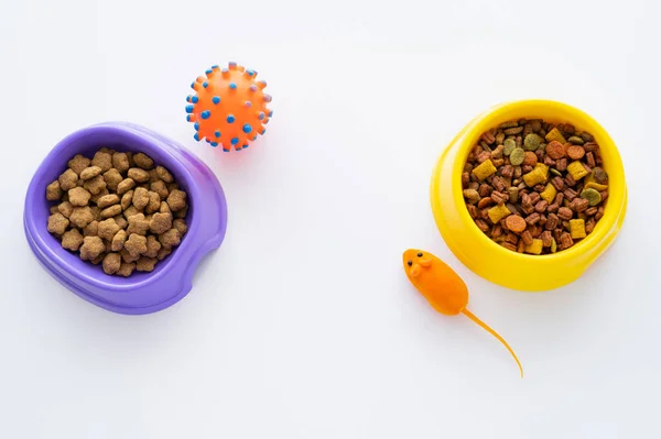 Vue de dessus de différents aliments secs pour animaux de compagnie dans des bols près de jouets isolés sur blanc — Photo de stock