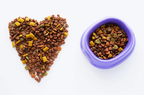 Top view of heart made of crunchy dry pet food and plastic bowl isolated on white — Stock Photo