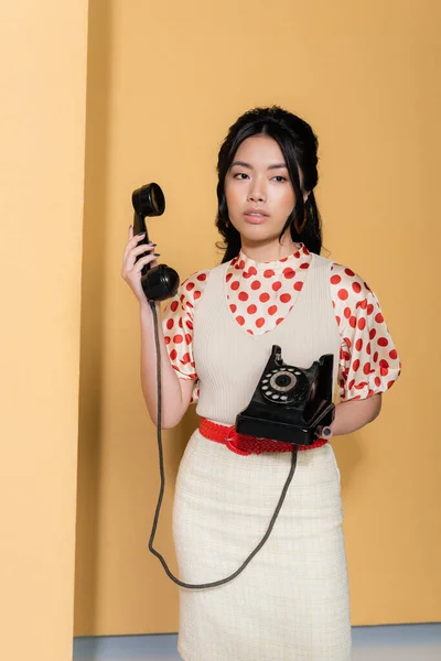 Modelo asiático em roupas vintage segurando telefone no fundo laranja — Fotografia de Stock
