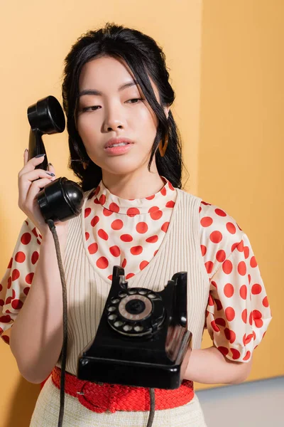 Elegante mujer asiática sosteniendo teléfono retro sobre fondo naranja - foto de stock