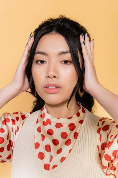 Retrato de mulher asiática elegante tocando cabelo isolado em laranja — Fotografia de Stock