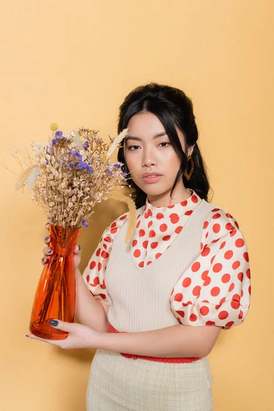 Elegante asiático modelo segurando vaso e flores no fundo laranja — Fotografia de Stock
