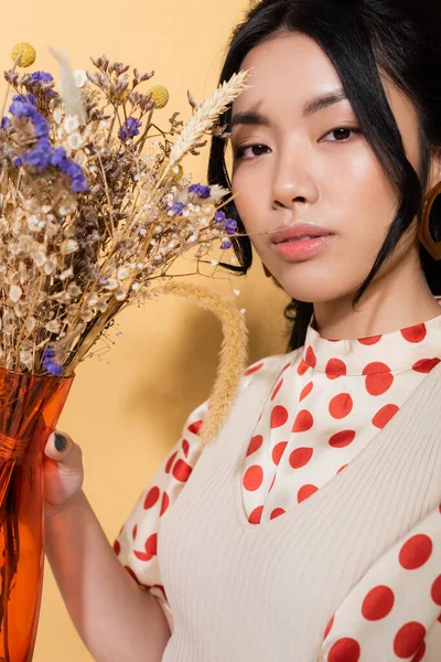 Portrait de modèle asiatique élégant tenant vase avec des fleurs sur fond orange — Photo de stock