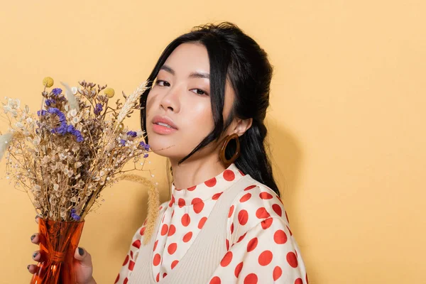 Femme asiatique à la mode en vêtements vintage tenant des fleurs sur fond orange — Photo de stock