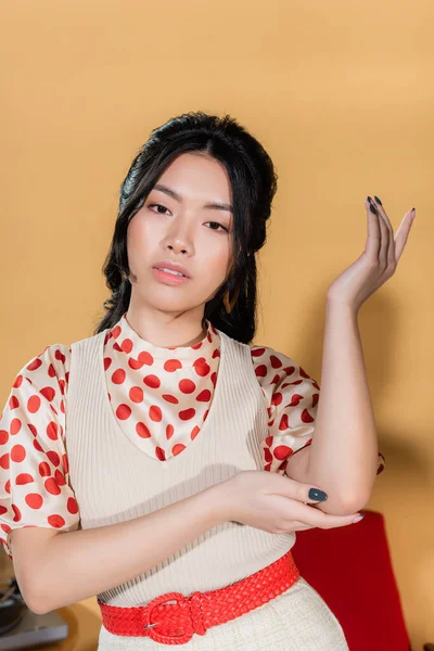 Elegante modelo asiático en ropa retro posando sobre fondo naranja - foto de stock