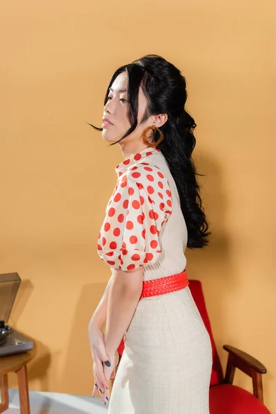 Junge asiatische Frau in Vintage-Klamotten schaut weg auf orangefarbenem Hintergrund — Stockfoto