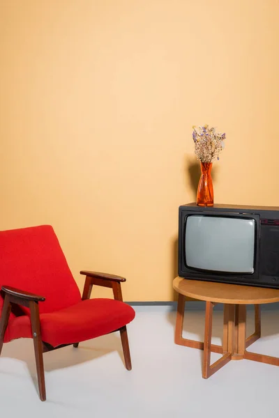 Fauteuil près de la télévision et des fleurs sur la table basse sur fond orange — Photo de stock