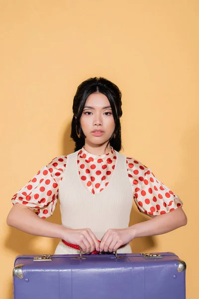 Asian model in dress holding vintage suitcase on orange background — Stock Photo