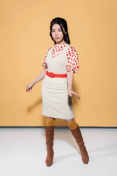 Full length of trendy asian model in retro clothes looking at camera on orange background — Stock Photo