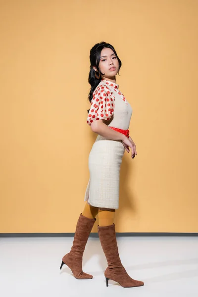 Досить азіатська жінка в блузці і одязі дивиться на камеру на помаранчевому фоні — стокове фото