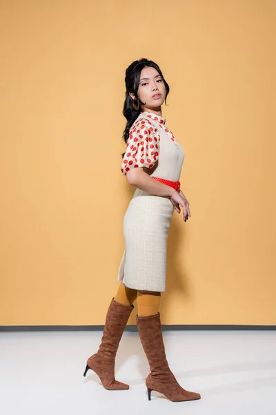 Bastante asiático mujer en blusa y vestido mirando cámara en naranja fondo - foto de stock