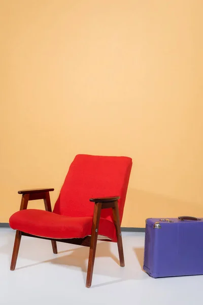 Vintage armchair near suitcase on orange background — Stock Photo