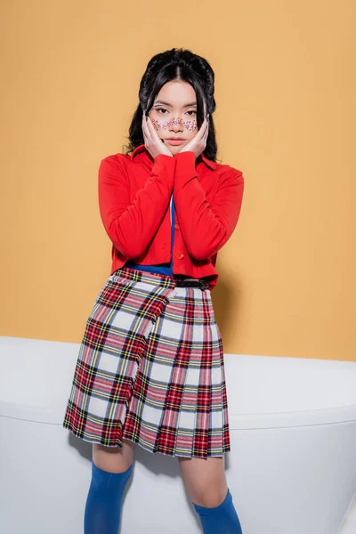 Stylish asian woman in retro clothes standing near bathtub on orange background — Stock Photo