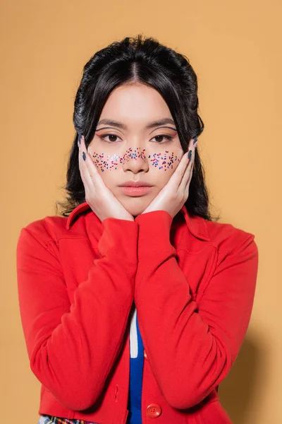 Portrait of asian woman with glitter on face looking at camera on orange background — Stock Photo