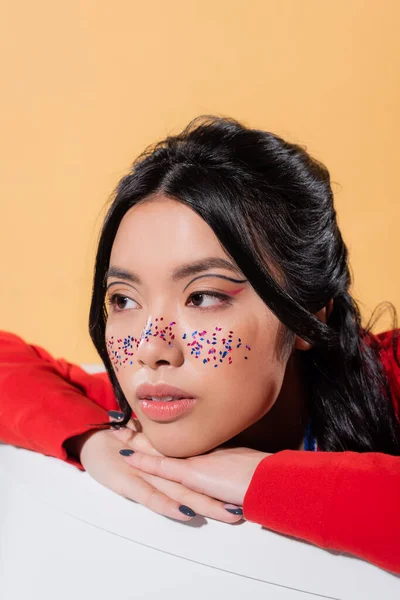 Pretty asian model with glitter on face sitting in bathtub isolated on orange — Stock Photo