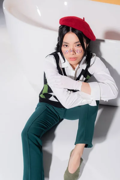 High angle view of pretty asian woman in beret looking at camera near bathtub on orange background — Stock Photo