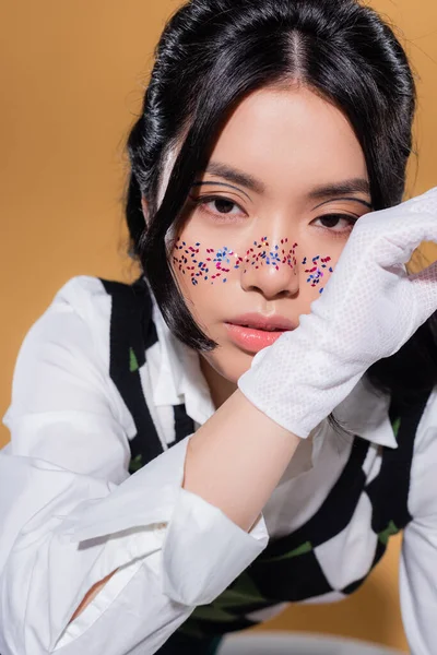 Porträt eines modischen asiatischen Models mit Glitzerschminke vor der Kamera auf orangefarbenem Hintergrund — Stockfoto