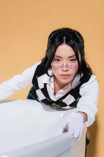 Portrait de femme asiatique élégante regardant la caméra près de la baignoire sur fond orange — Photo de stock