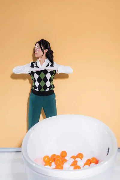 Stylish asian model in vintage clothes posing near bathtub with balls on orange background — Stock Photo