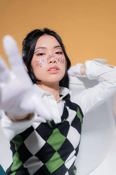 Portrait de modèle asiatique élégant en gants regardant la caméra près de la baignoire isolé sur orange — Photo de stock