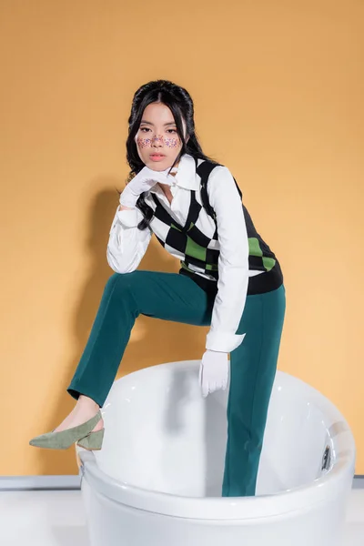 Pretty asian woman in vintage clothes and gloves posing in bathtub on orange background — Stock Photo