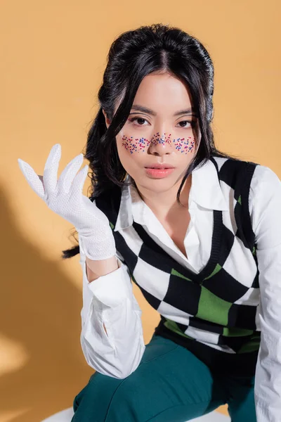 Elegante modelo asiático con maquillaje posando sobre fondo naranja - foto de stock