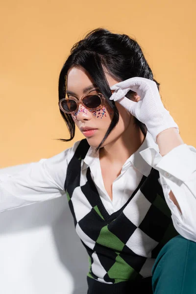 Fashionable model in sunglasses sitting in bathtub isolated on orange — Stock Photo