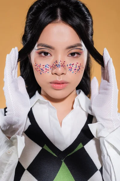 Retrato de modelo asiático con maquillaje posando y mirando a la cámara aislada en naranja - foto de stock