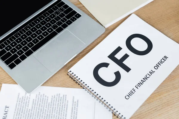 High angle view of laptop near notebook with cfo lettering and contract on desk — Stock Photo