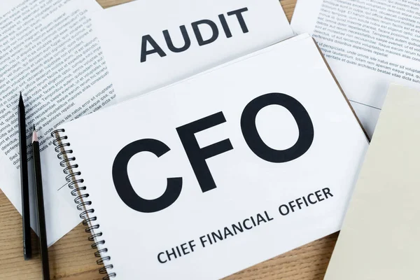 Top view of notebook with cfo abbreviation near paper with audit lettering on desk — Stock Photo