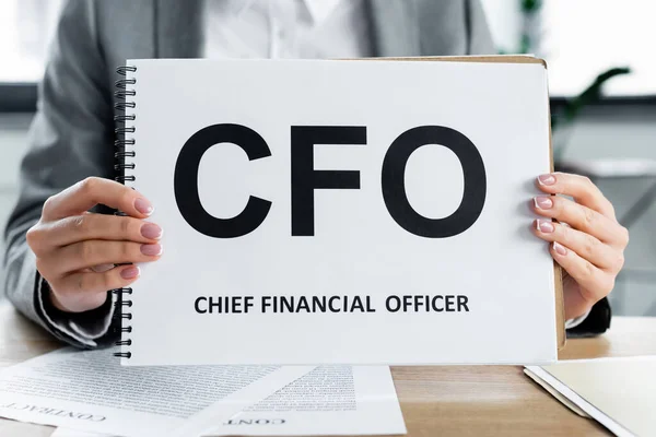 Vista recortada de la mujer de negocios que sostiene el cuaderno con letras cfo en la oficina - foto de stock