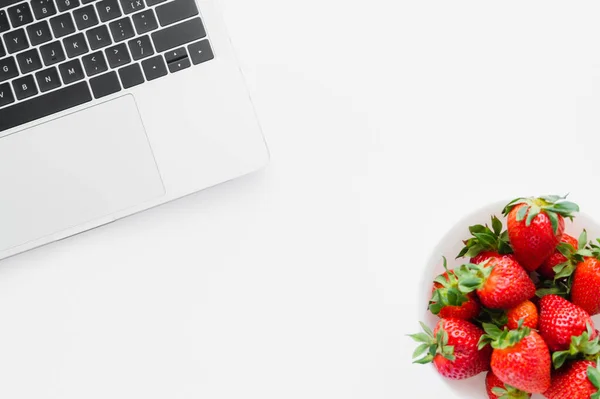 Vue de dessus des fraises naturelles près de l'ordinateur portable sur fond blanc — Photo de stock