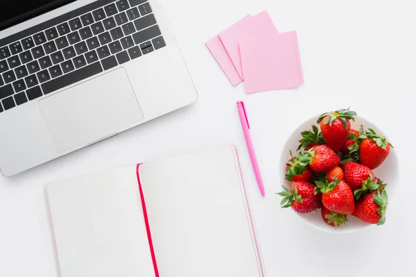 Vista superior do laptop perto de notebook e morangos saborosos no fundo branco — Fotografia de Stock