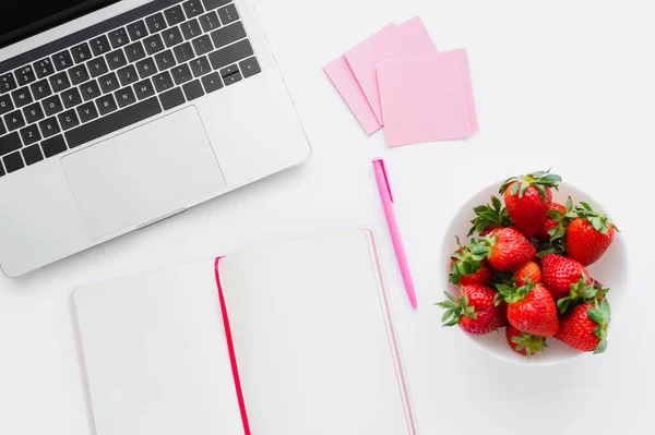 Vista superior de la computadora portátil cerca del cuaderno y sabrosas fresas sobre fondo blanco - foto de stock