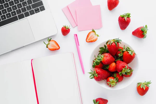 Ansicht von Bio-Erdbeeren in der Nähe von Laptop und Notizbuch auf weißem Hintergrund — Stockfoto