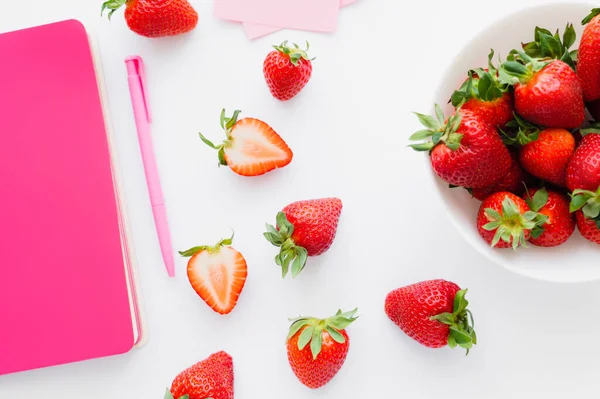 Top view of natural strawberries near pink pen and notebook on white background — Stock Photo