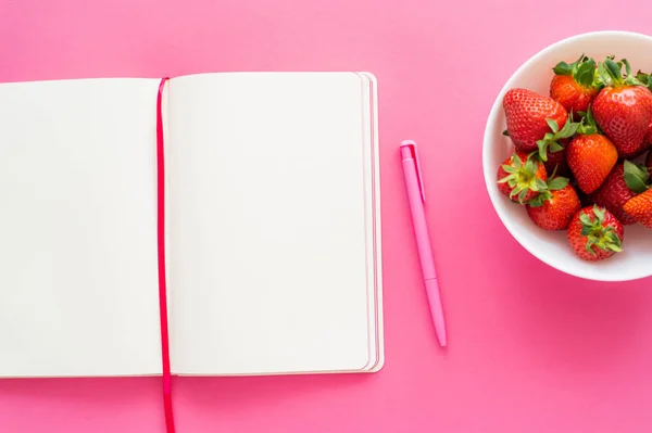 Top view of open notebook with pen and fresh strawberries on pink background — Stock Photo