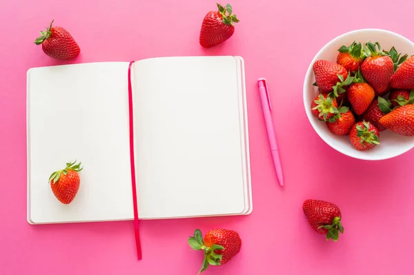 Vue du dessus des fraises naturelles près du carnet ouvert sur fond rose — Photo de stock