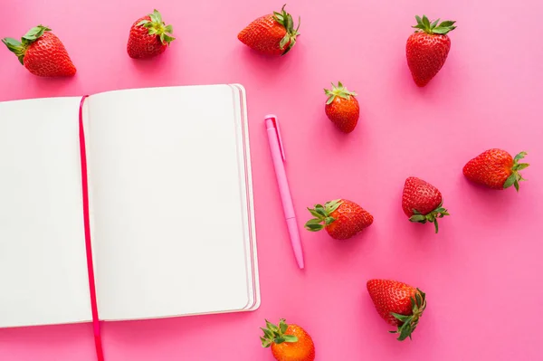 Vista superior de morangos orgânicos e caderno aberto em fundo rosa — Fotografia de Stock